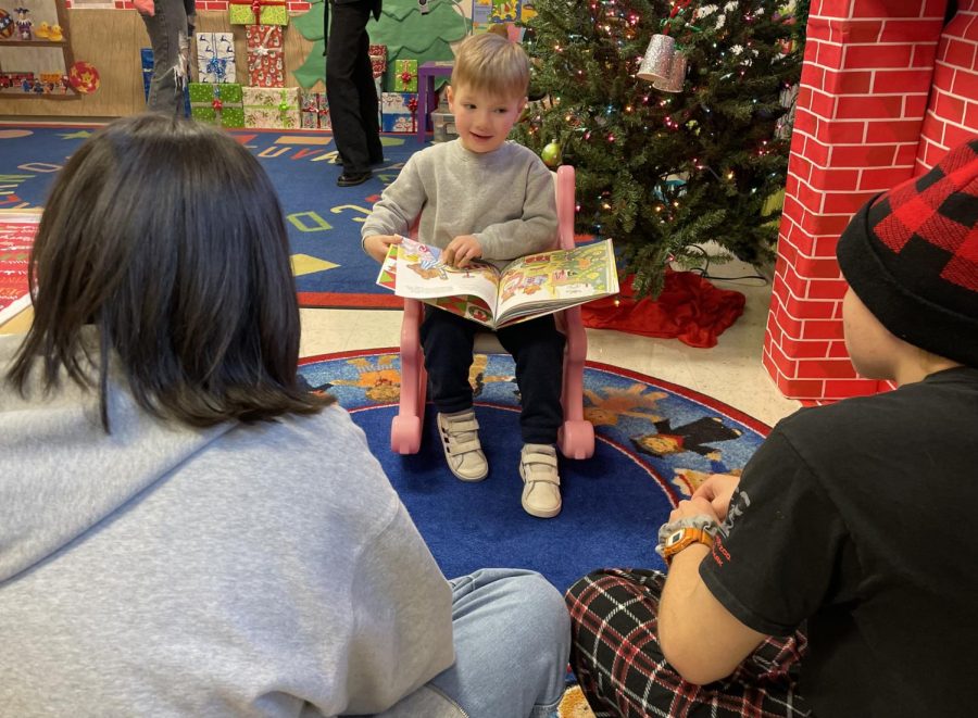 A preschool student reads a book to his ECE buddies. 