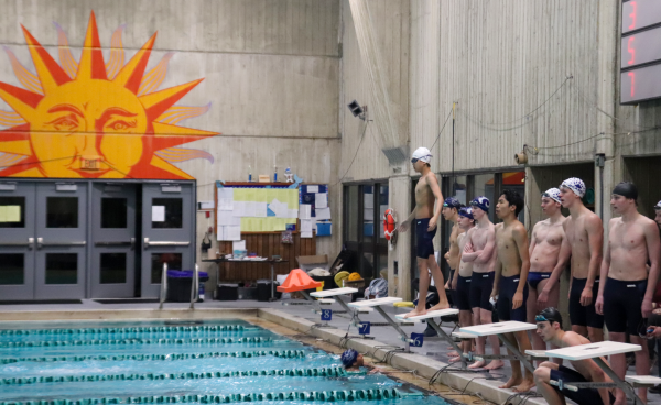 Steve Su, Kasey Gridley, and Jack Fuller stand behind lane five as Scott Hermann finishes the 400 Freestyle Relay against Rogers High School.
